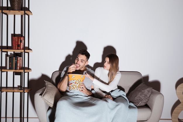 Young Woman And Man Watching Tv And Eating Popcorn On Sofa