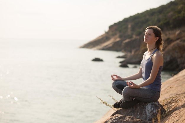 Premium Photo | Young woman meditating on the rock near to seaside ...