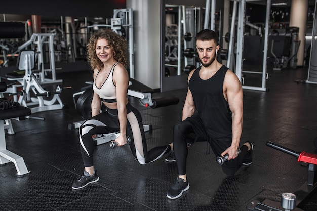 Young woman and personal trainer with dumbbell squats in gym Free Photo