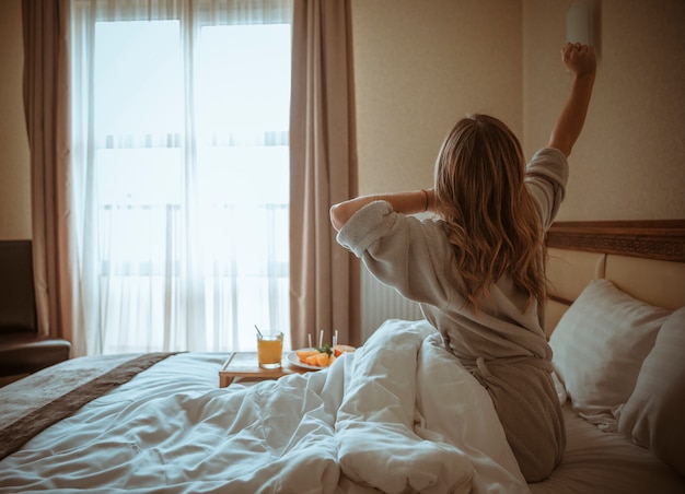 Young Woman Sitting On Bed Stretching Her Hand With