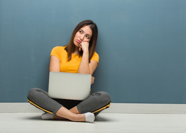 Young woman sitting on the floor with a laptop thinking of something, looking to the side Premium Photo