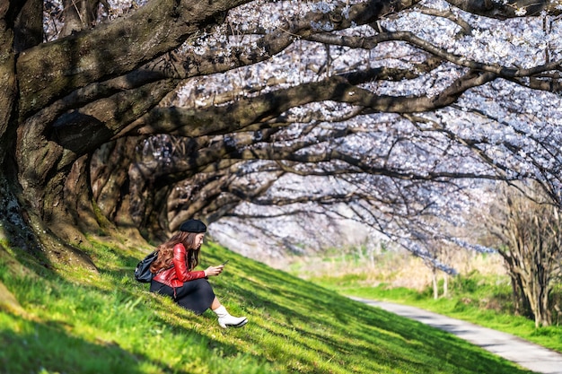 春の日に桜の庭に座っている若い女性 日本の京都の桜の木を漕ぐ 無料の写真