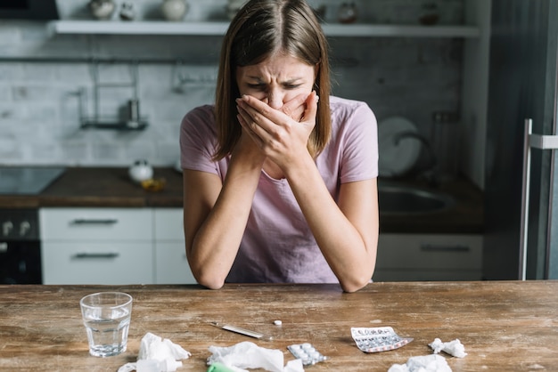 Young woman suffering from nausea with medicines and glass of water on desk Free Photo