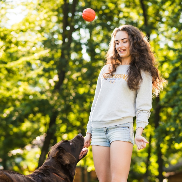 Free Photo Young woman throwing ball for her dog at park