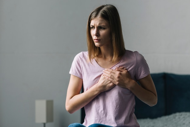 Young woman touching her chest in pain at home | Free Photo