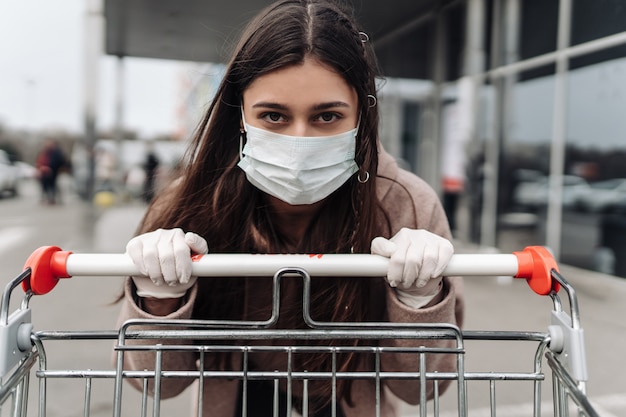 Young woman wearing protection face mask against coronavirus 2019-ncov pushing a shopping cart. Free Photo