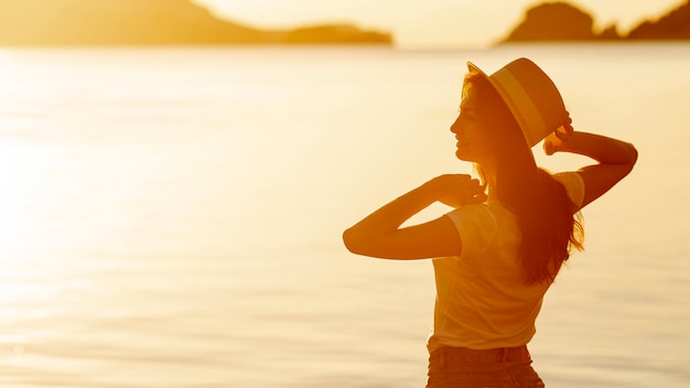 Premium Photo | Young woman with a hat at sunset on the shore of a lake