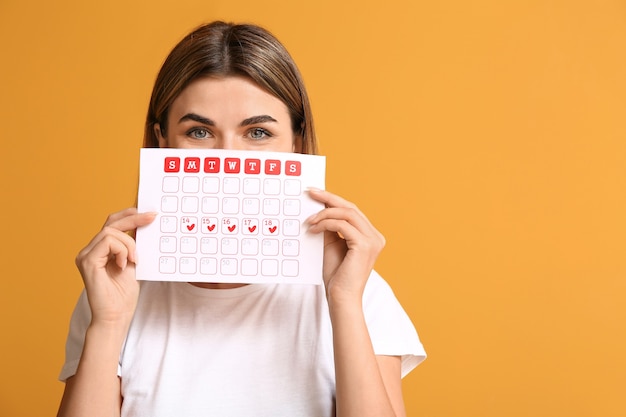 Young woman with menstrual calendar on color surface Premium Photo