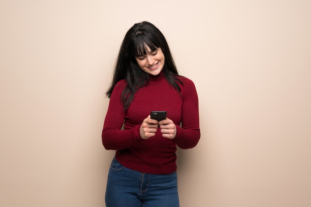 Young woman with red turtleneck sending a message with the mobile Premium Photo