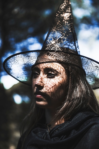 Free Photo | Young woman in wizard hat and cloak looking away in forest