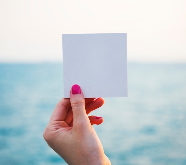 Hand holding perforated paper frame with ocean background Free Psd