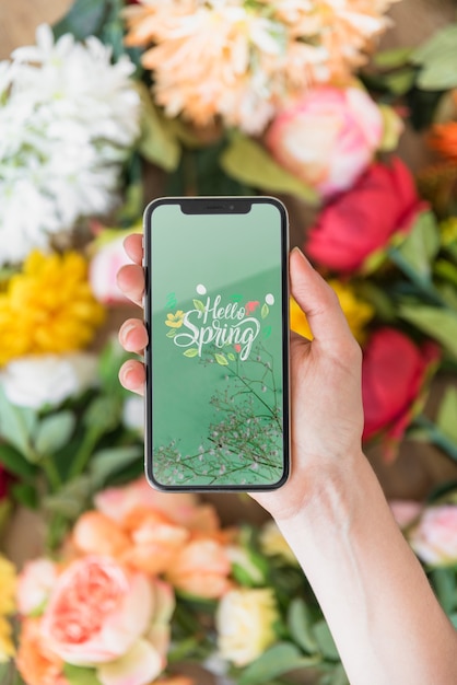 Download Hand holding smartphone mockup above flowers | Free PSD File