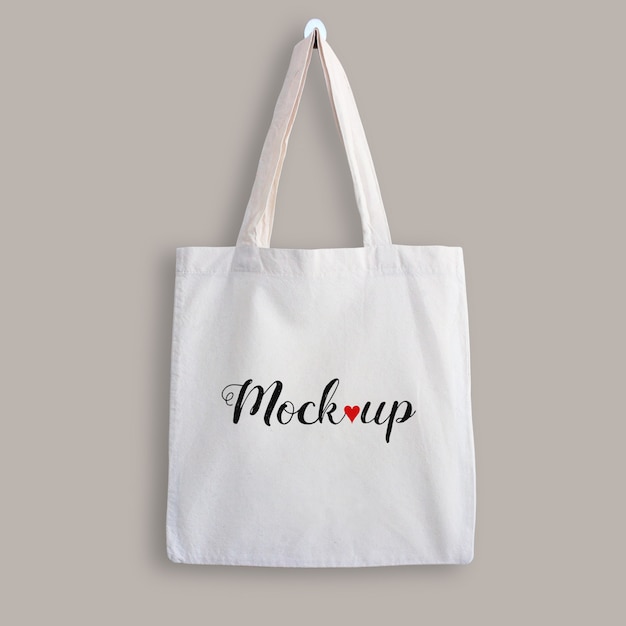 Download Mockup of a white cotton tote bag hanging on a wall | Premium PSD File