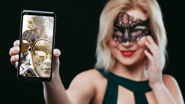 Woman with carnival mask showing smartphone mockup PSD Template