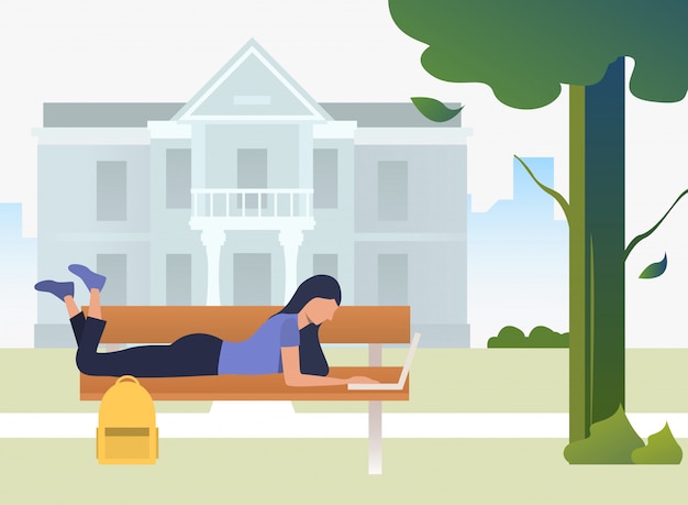 Student studying, using laptop and lying on bench in campus park Free Vector