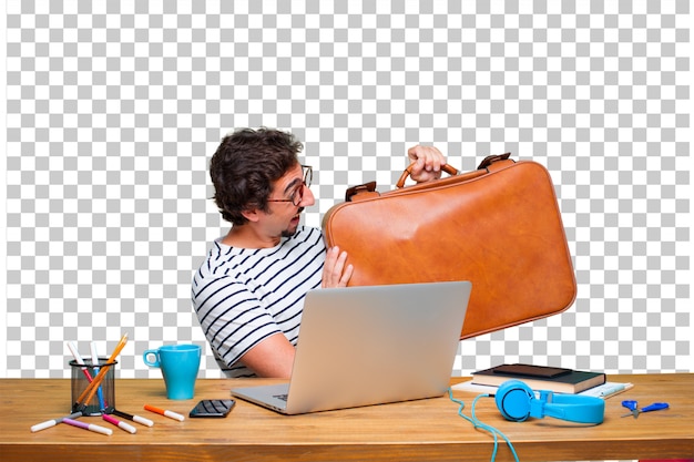 Junger verrückter grafikdesigner auf einem schreibtisch mit einem laptop und mit einem lederkoffergepäck Premium PSD