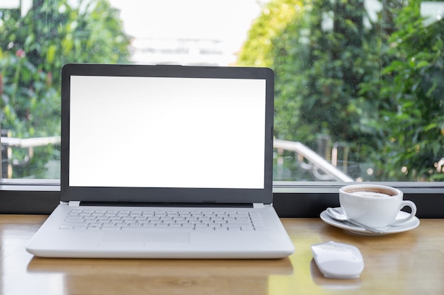 Verspotten sie herauf leeren bildschirm des laptops mit einer kaffeetasse auf holztisch mit beschneidungspfad unscharfem hintergrund. Premium PSD