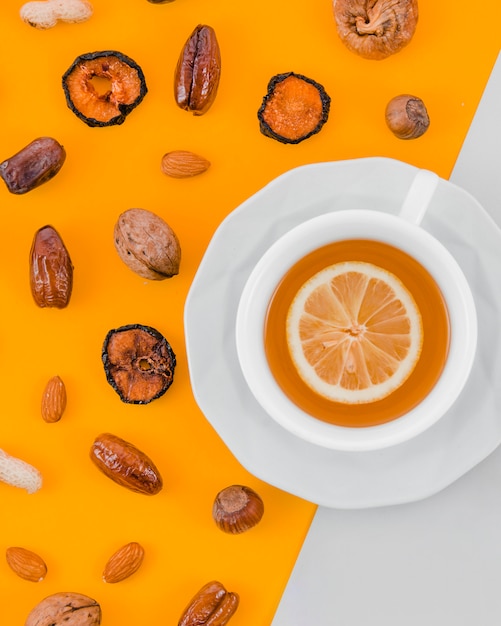 Abricot sec; rendez-vous; amandes; noyer; cacahuète et noisette avec une tasse de thé au citron sur fond jaune et blanc Photo gratuit