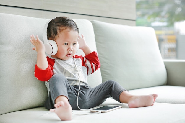 Adorable Petit Bebe Garcon Assis Sur Un Canape Et Ecouter De La Musique Au Casque Par Smartphone Photo Premium