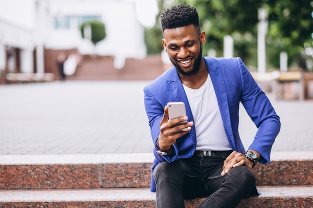 Afro-américain en veste bleue à l'aide de téléphone Photo gratuit