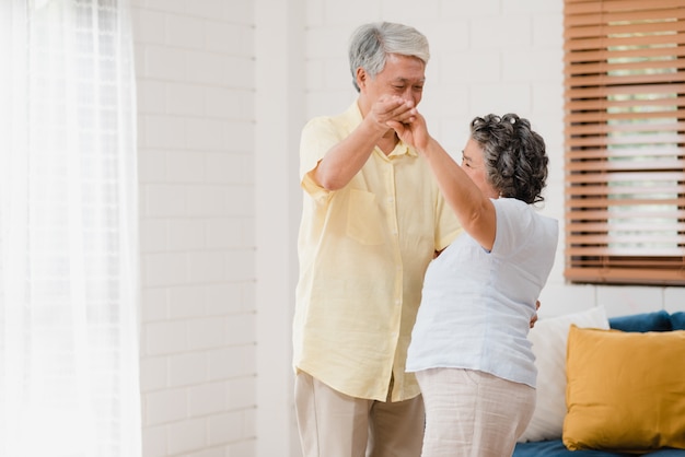 Asiatique couple de personnes âgées danser ensemble tout en écoutant de la musique dans le salon à la maison, couple adorable profiter d'un moment d'amour tout en s'amusant quand il est détendu à la maison. Photo gratuit