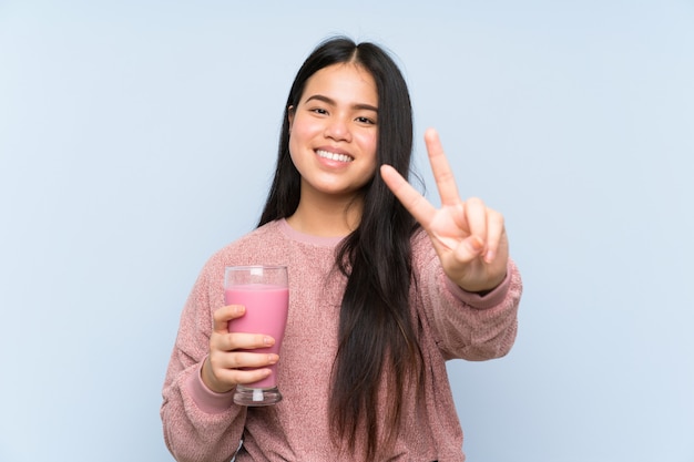 Asiatique jeune adolescente avec milkshake à la fraise souriant et montrant le signe de la victoire Photo Premium
