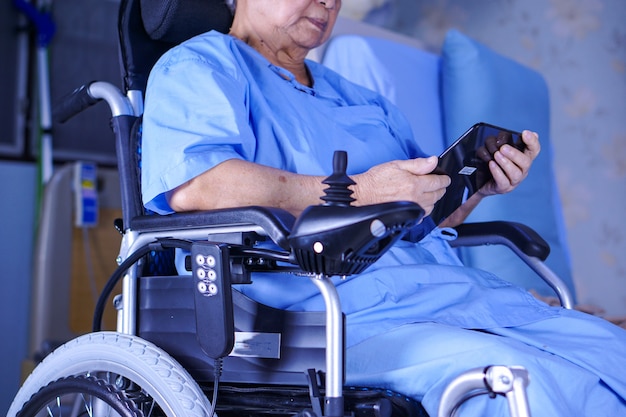 Asiatique senior ou âgée vieille dame patiente tenant dans ses mains une tablette numérique et lire des emails tout en restant assise sur son lit dans un hôpital de soins infirmiers Photo Premium
