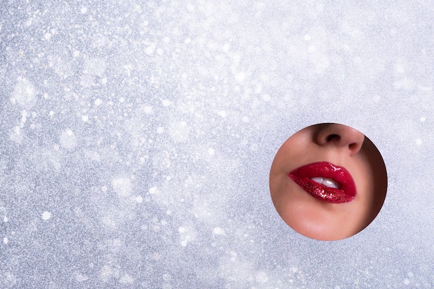 Bannière publicitaire de salon de beauté avec espace de copie. vue de lèvres brillantes avec des paillettes à travers le trou dans le fond de papier argenté. Photo Premium