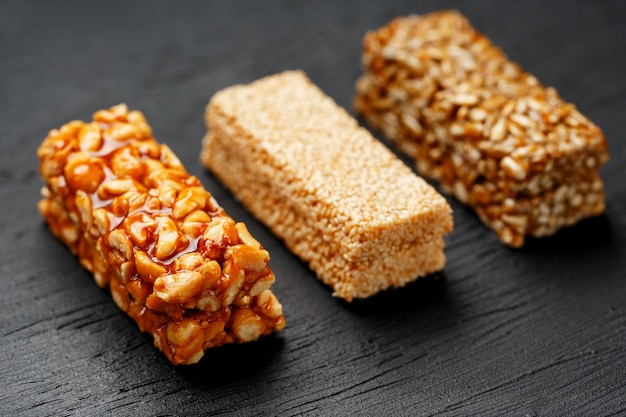 Barre granola de céréales avec des cacahuètes, des graines de sésame et de tournesol sur une planche à découper sur une table en pierre sombre. vue d'en-haut. trois barres assorties Photo Premium