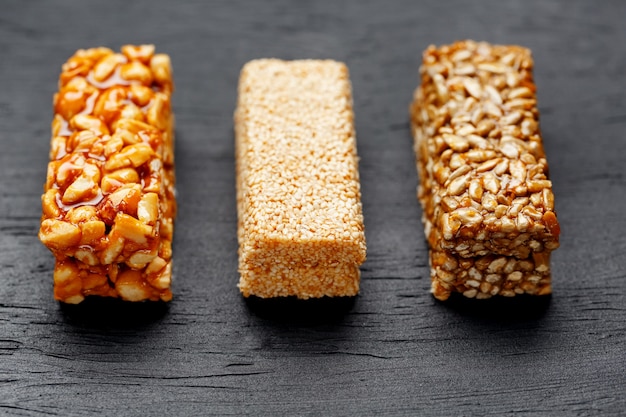 Barre granola de céréales avec des cacahuètes, des graines de sésame et de tournesol sur une planche à découper sur une table en pierre sombre. vue d'en-haut. trois barres assorties Photo Premium