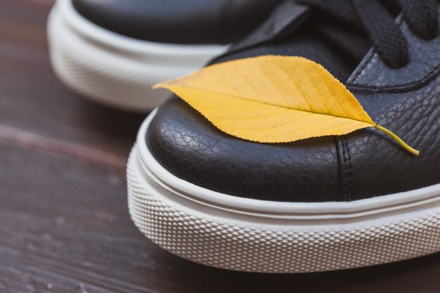 Baskets en cuir noir avec une feuille jaune sur fond en bois. concept d'automne Photo Premium