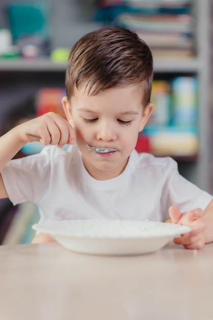 Beau Garcon Mange De La Bouillie De Lait Joli Bebe Prenant Son Petit Dejeuner Assis A Une Table Dans La Cuisine A La Maison Photo Premium