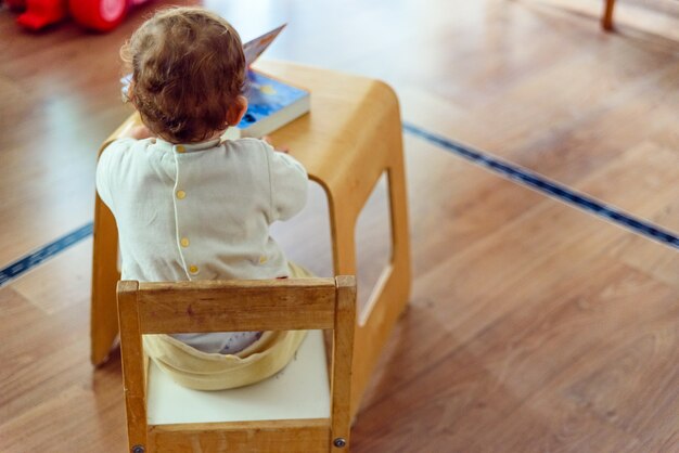 Bebe De 1 An Assis Sur Son Dos Sur Une Chaise Pour Lire Un Livre Photo Premium