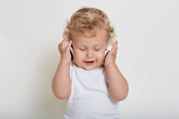 Bebe Blond Aux Cheveux Boucles Avec Un Casque Sur L Espace Blanc Enfant Appreciant La Musique Avec Les Yeux Fermes Photo Premium