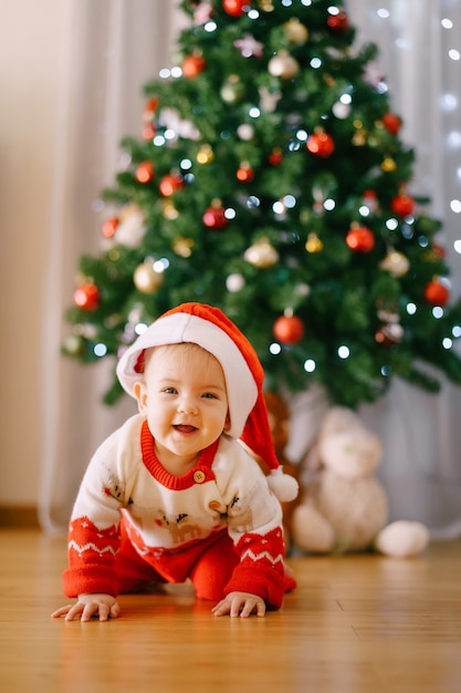 Bebe Dans Un Costume De Renne Tricote Et Bonnet De Noel Rampe Devant Un Arbre De Noel Photo De Haute Qualite Photo Premium