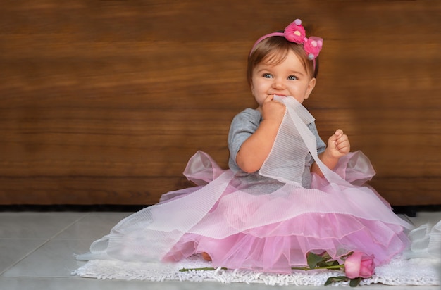 Bebe Dans Une Robe Et Des Rubans Sur Un Fond En Bois Un Enfant Dans Une Robe Rose Mord Un Ruban Blanc Sur Un Fond De Bois Photo Premium