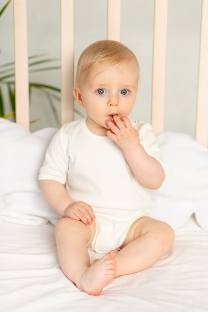 Bebe Garcon Blond Aux Yeux Bleus Dans Un Body Blanc Sur Un Lit Avec Des Sous Vetements En Coton A La Maison Avant D Aller Au Lit Photo Premium