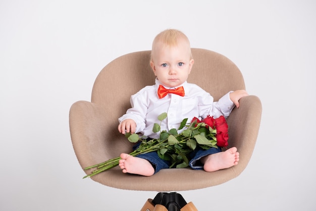 Bebe Garcon En Costume Et Nœud Papillon Rouge Detient Bouquet De Roses Est Assis Dans Une Chaise Sur Un Fond Blanc Photo Premium