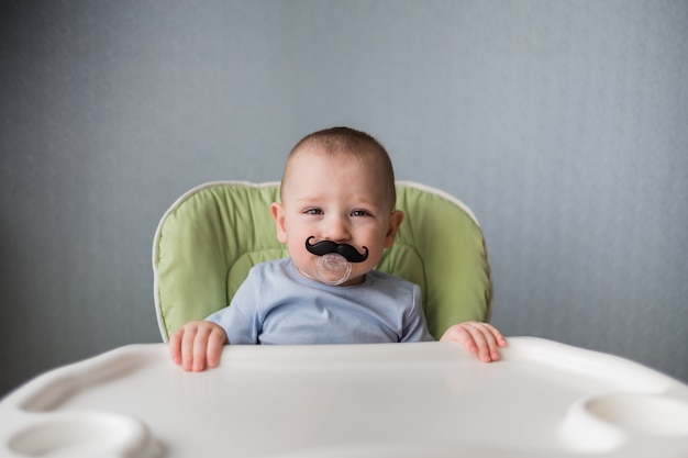 Bebe Avec Une Tetine En Forme De Moustache Est Assis Sur Une Chaise Haute Photo Premium