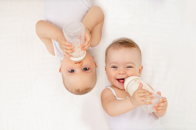 Bebes Jumeaux Garcon Et Fille Avec Une Bouteille De Lait Sur Un Lit Blanc A La Maison Concept De Nourriture Pour Bebe Photo Premium