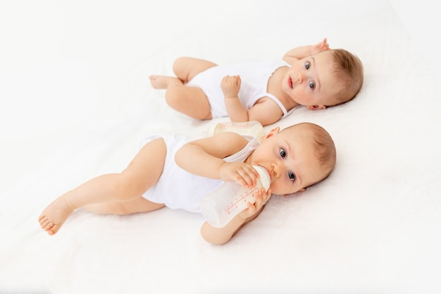 Bebes Jumeaux Garcon Et Fille Avec Une Bouteille De Lait Sur Un Lit Blanc A La Maison Concept De Nourriture Pour Bebe Photo Premium