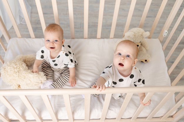 Des Bebes Jumeaux Sont Assis En Pyjama Dans Le Berceau Photo Premium