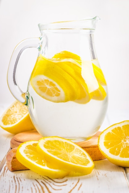 Un bécher en verre et un pichet de limonade froide sur un fond en bois blanc entouré de citrons. Photo Premium