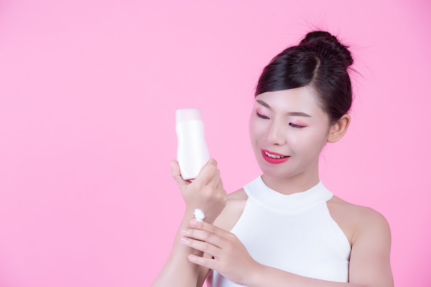Belle femme asiatique tenant une bouteille de produit sur un fond rose. Photo gratuit