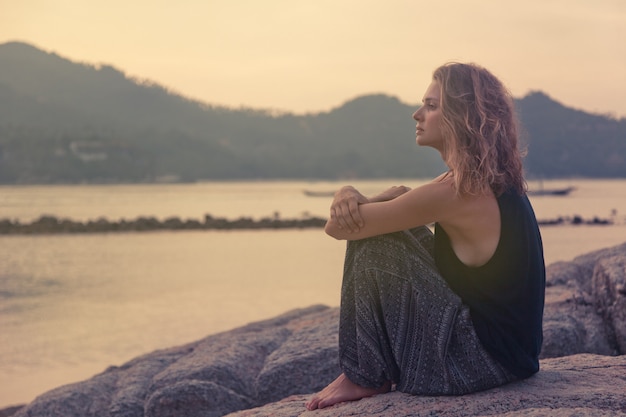 Belle Jeune Femme Assise Sur Les Rochers Au Bord De La Mer Et Regarder Le Coucher Du Soleil