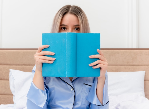 Belle Jeune Femme En Pyjama Bleu Assis Sur Le Lit Avec Un Livre Se