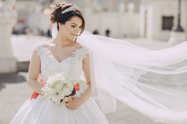 Belle mariée dans une robe blanche et une couronne sur sa tête dans un parc et tenant le bouquet Photo gratuit