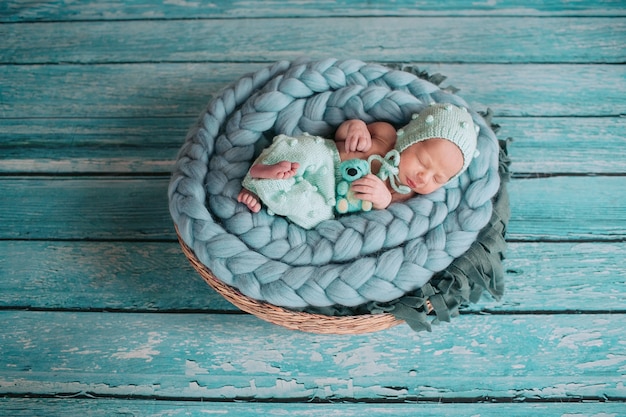Belle petite fille dort avec un ours bleu sur une couverture bleue dans le panier Photo gratuit