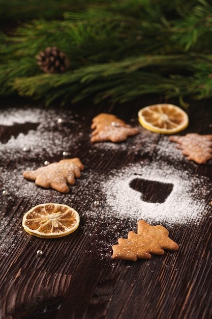 Biscuits De Pain D'épice En Forme De Sapin De Noël Et De Coeur, Sucre En Poudre Sur Une Table En Bois, Agrumes Séchés, Branche De Sapin, Angle De Vue, Mise Au Point Sélective Photo Premium