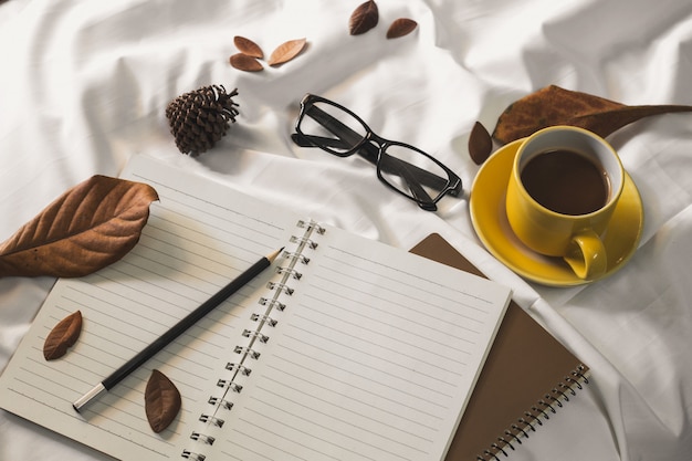 Bloc-notes lettre tasse de café et un livre avec une couverture sur un textile blanc au lit. Photo Premium